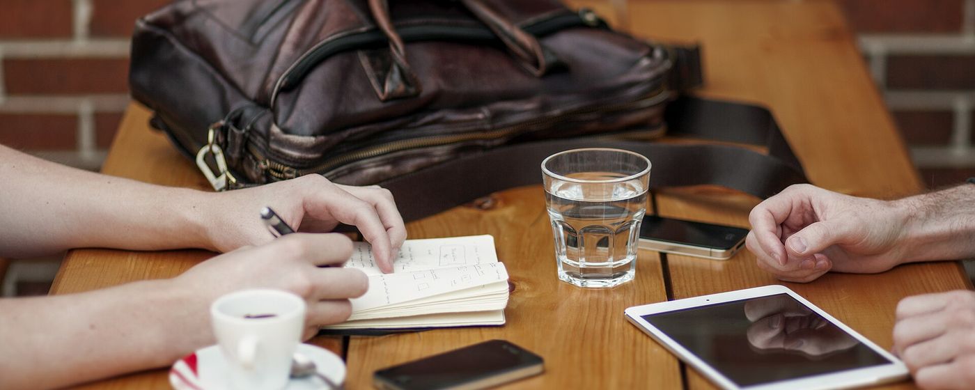 Two people at a table comparing notes on a notebook and a tablet