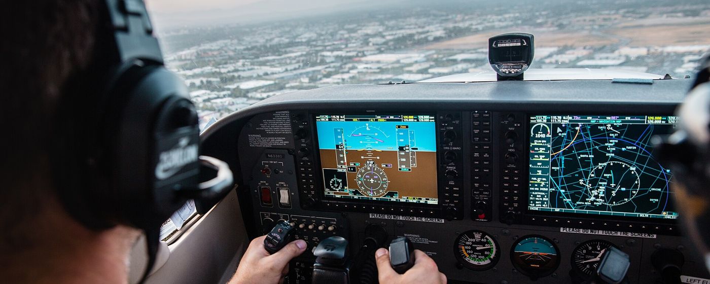 A pilot's hands on the controls of a small aircraft cockpit at sunset