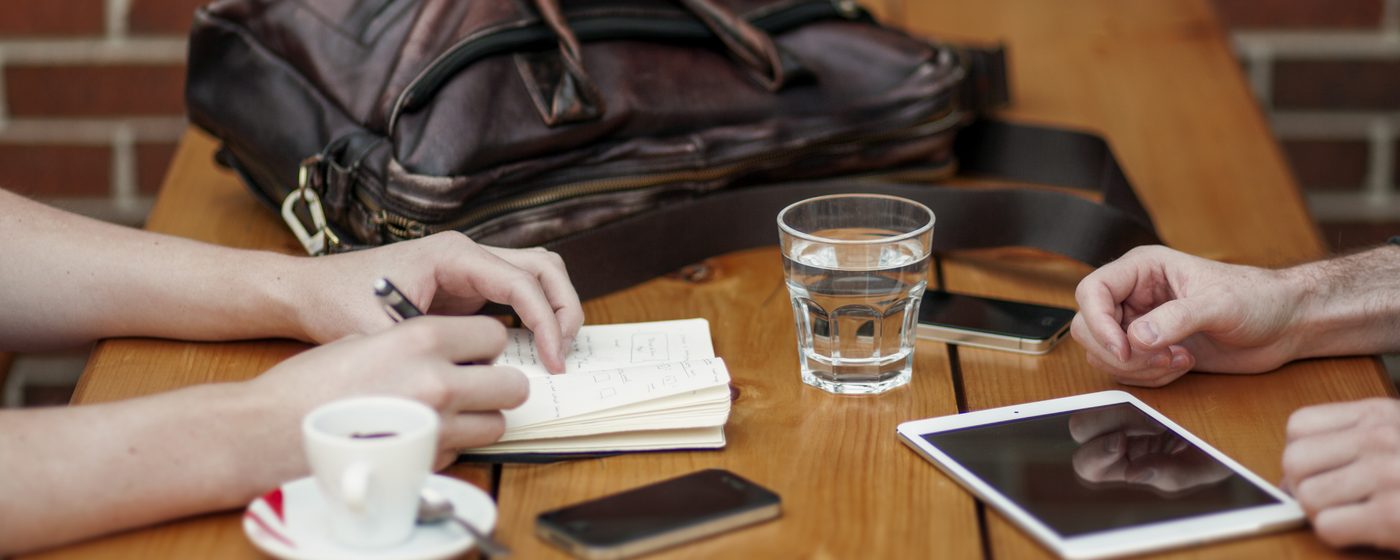 Two people at a table with a notebook, a tablet and coffee
