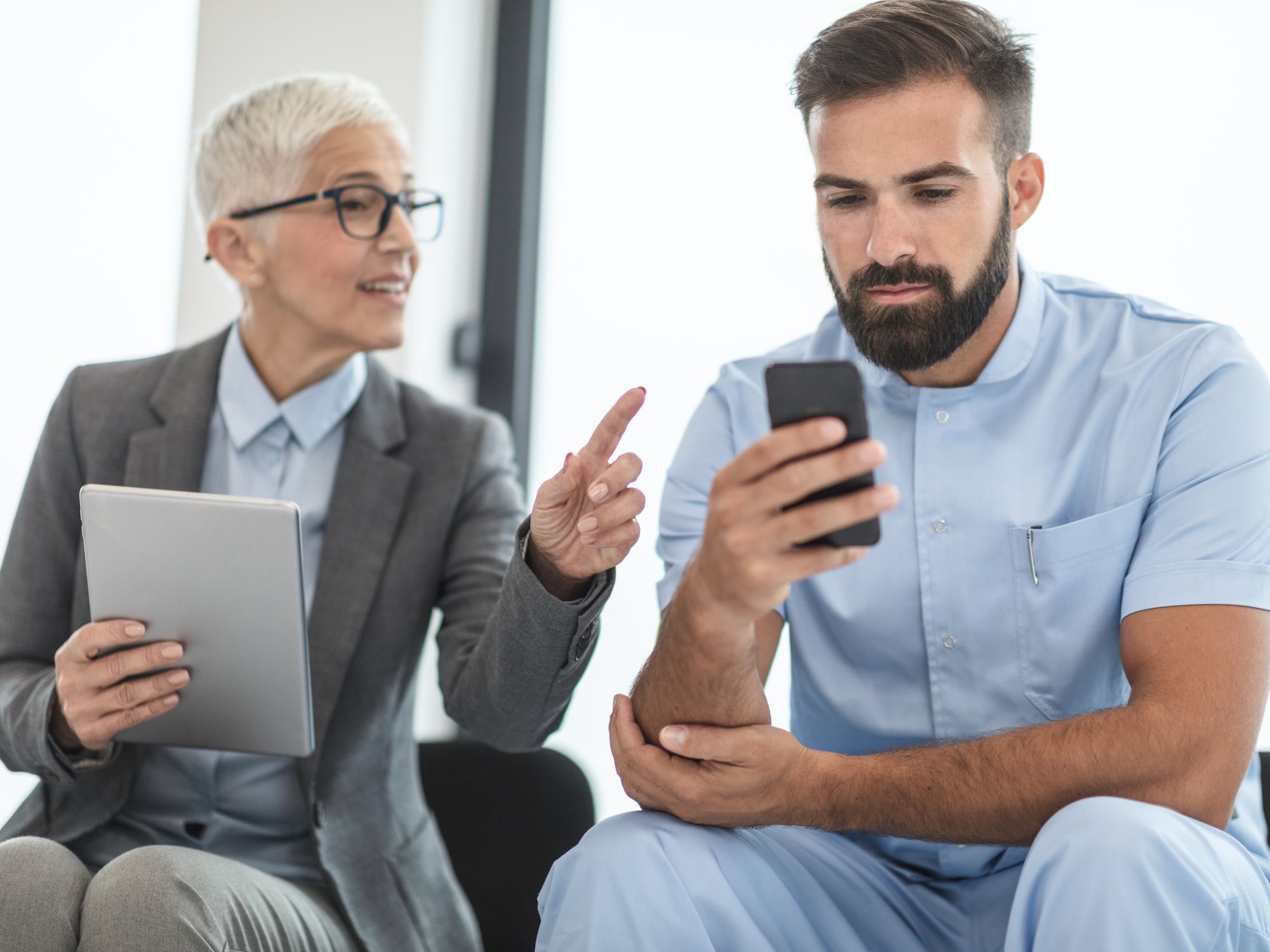 Two colleagues comparing notes on a tablet and a phone