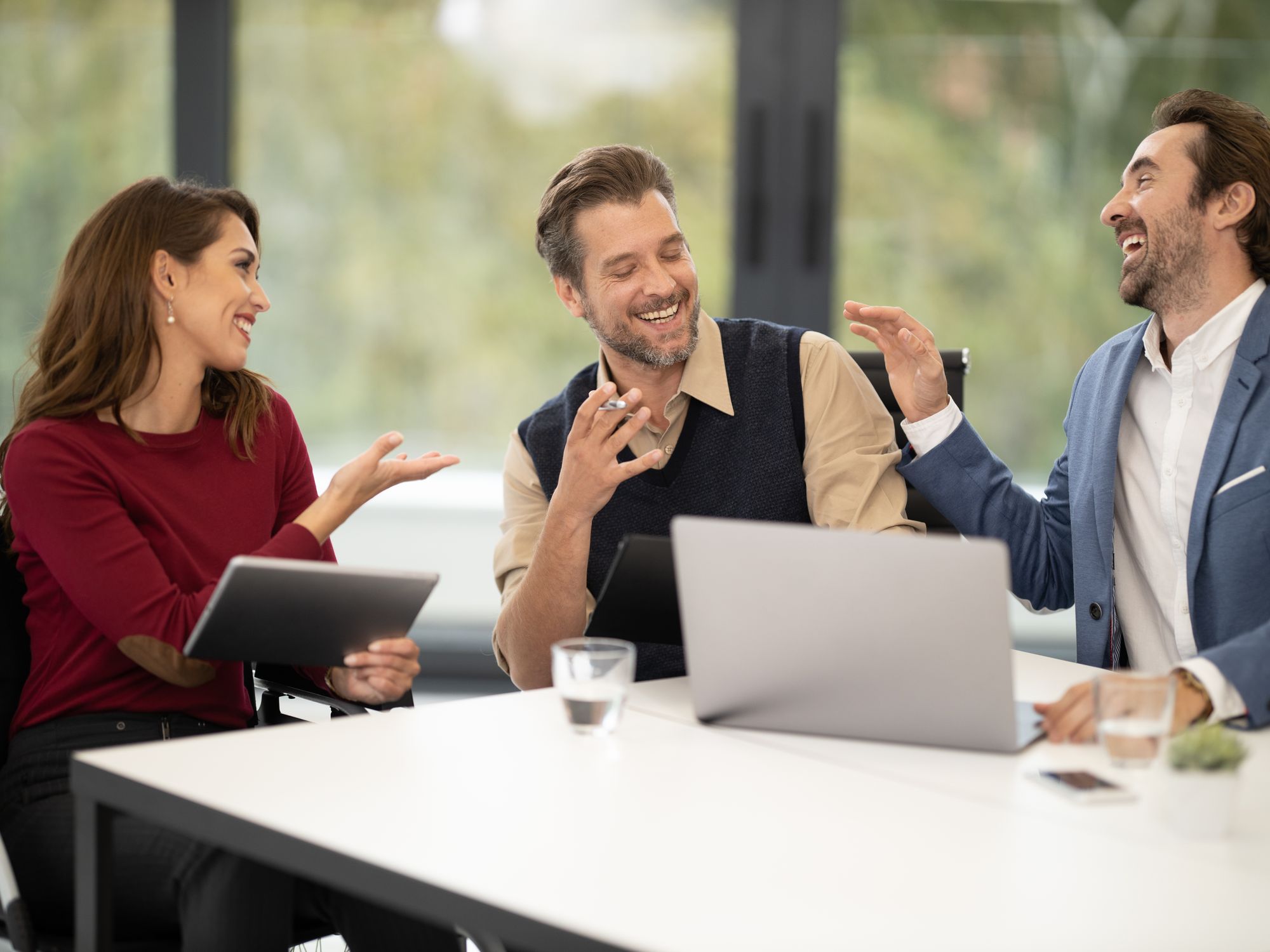 Three colleagues talking over a laptop at a white table