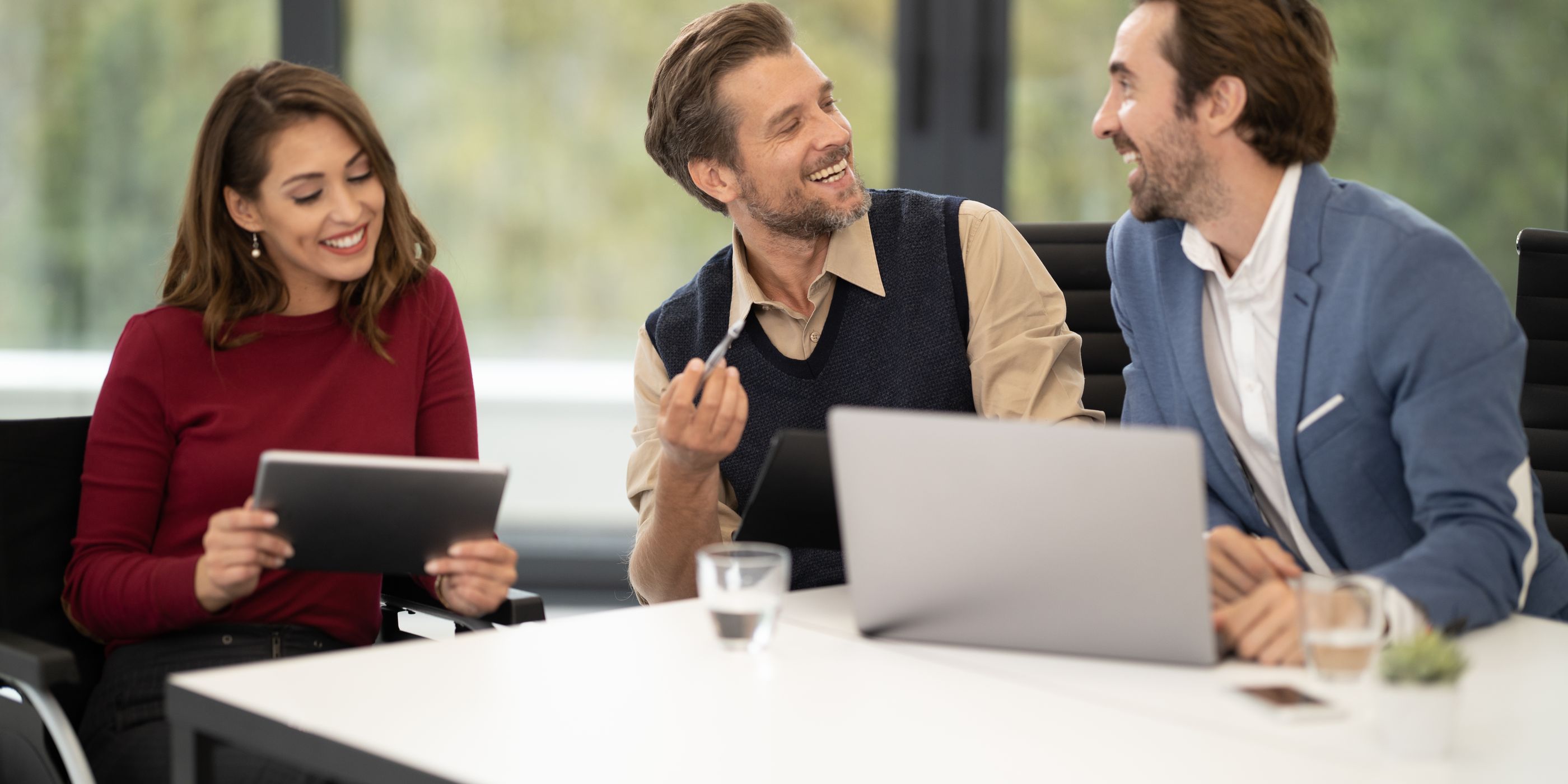 A woman with a tablet talking with two colleagues at a table