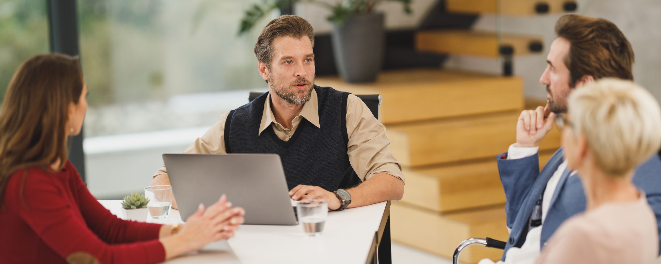Four colleagues in discussion at a table with a laptop