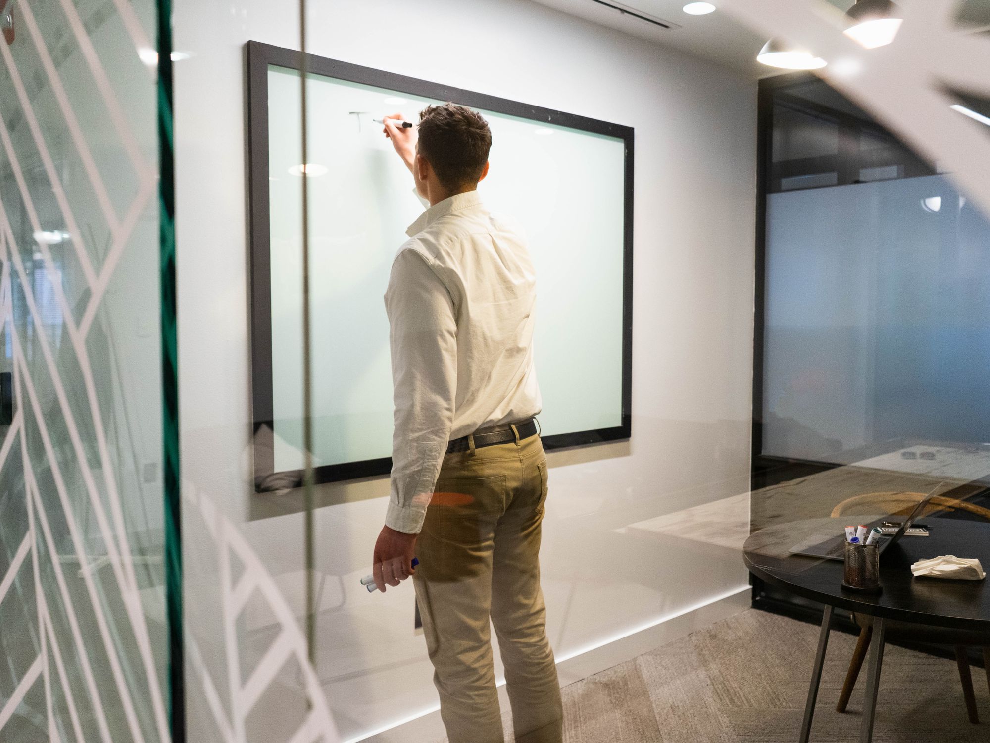 A man sketching on a glass wall in an office