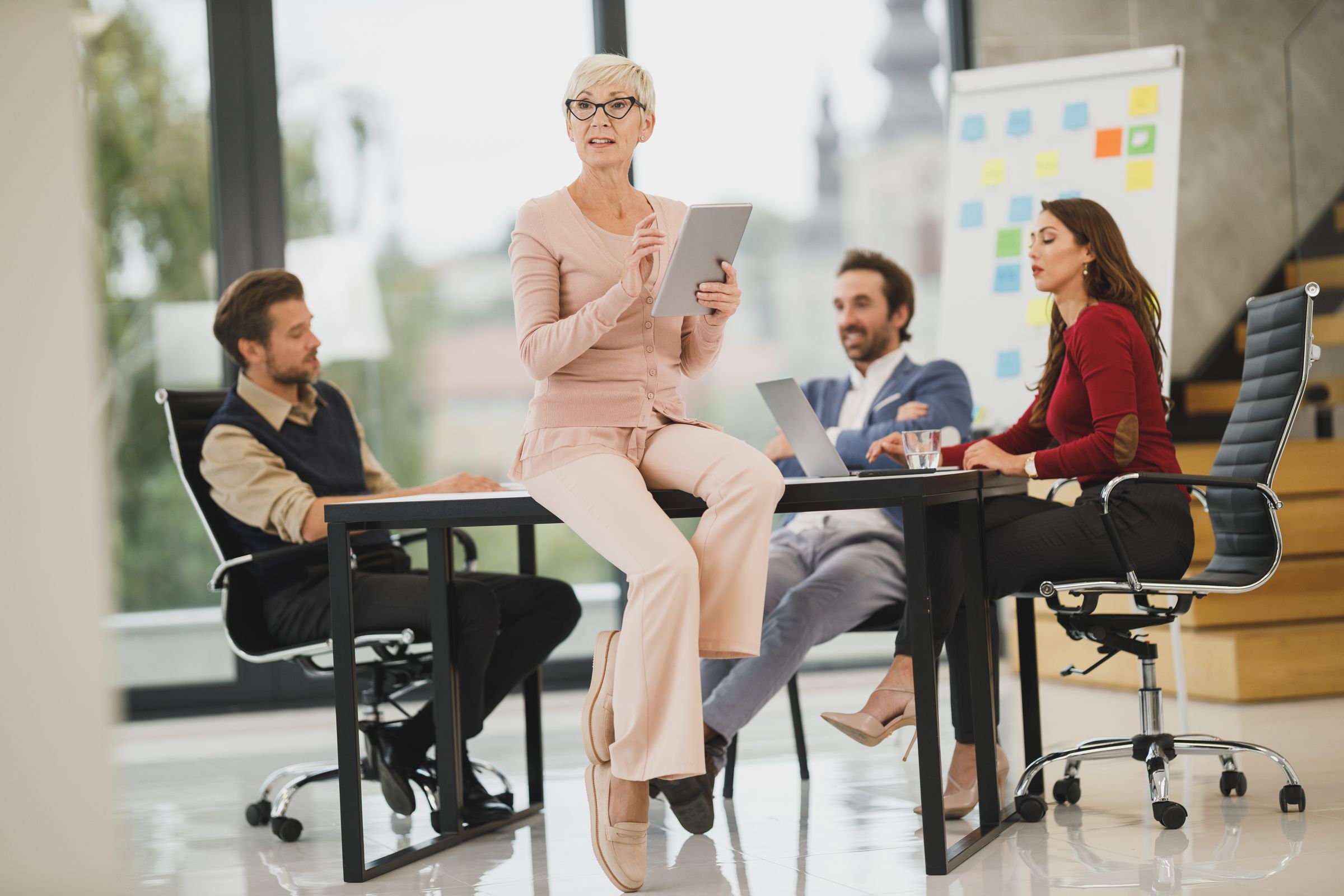 An older colleague standing with a tablet among her team