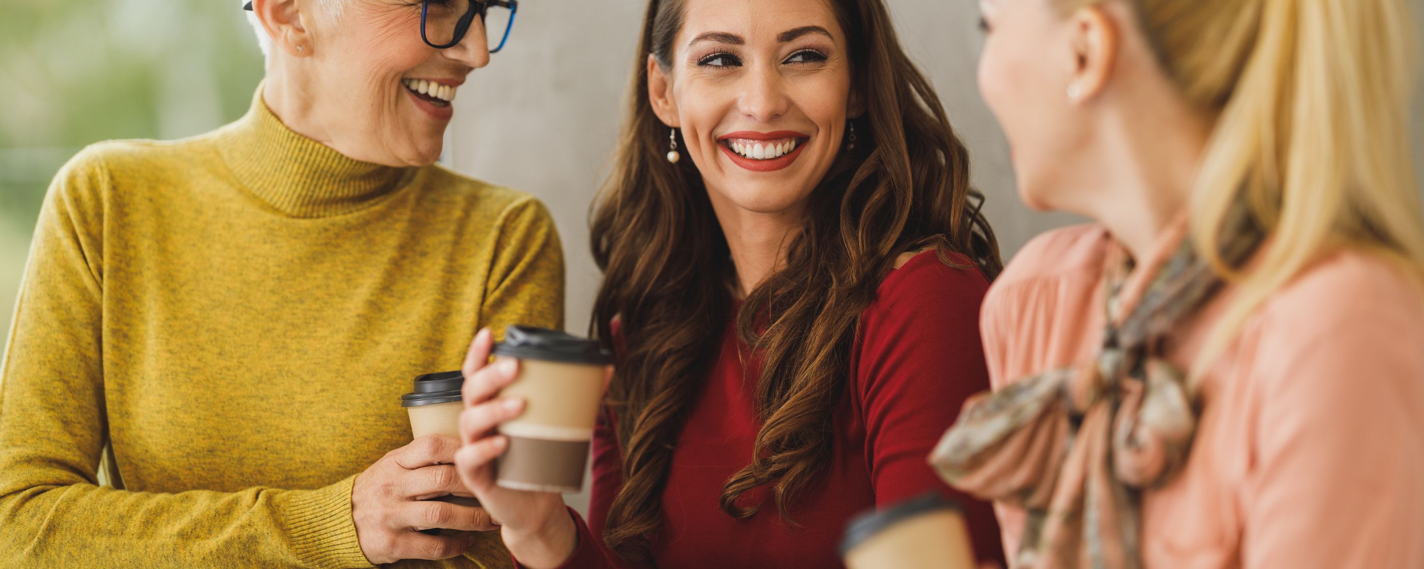 Three women colleagues laughing over coffee