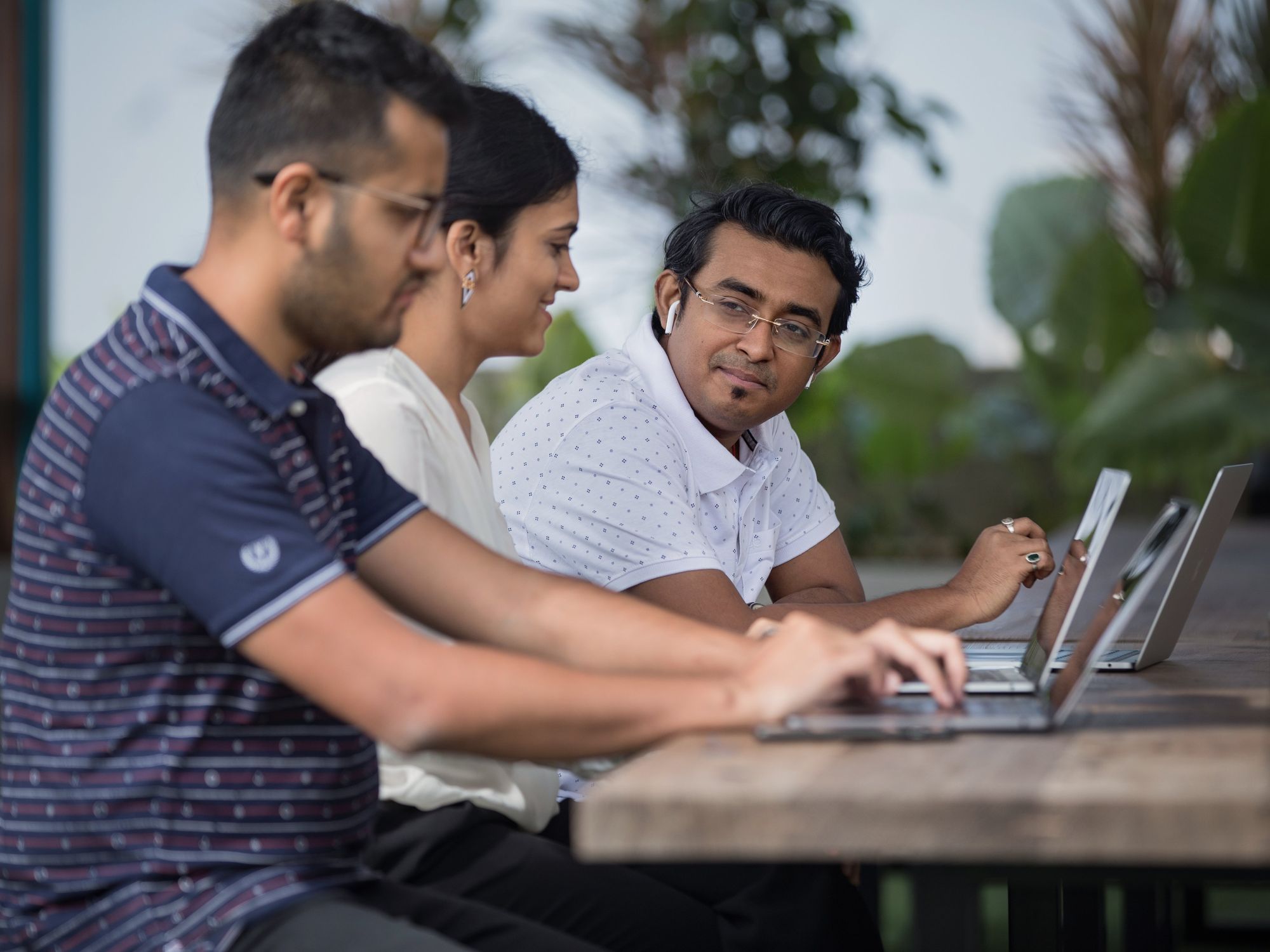 Three colleagues working on laptops at a bench