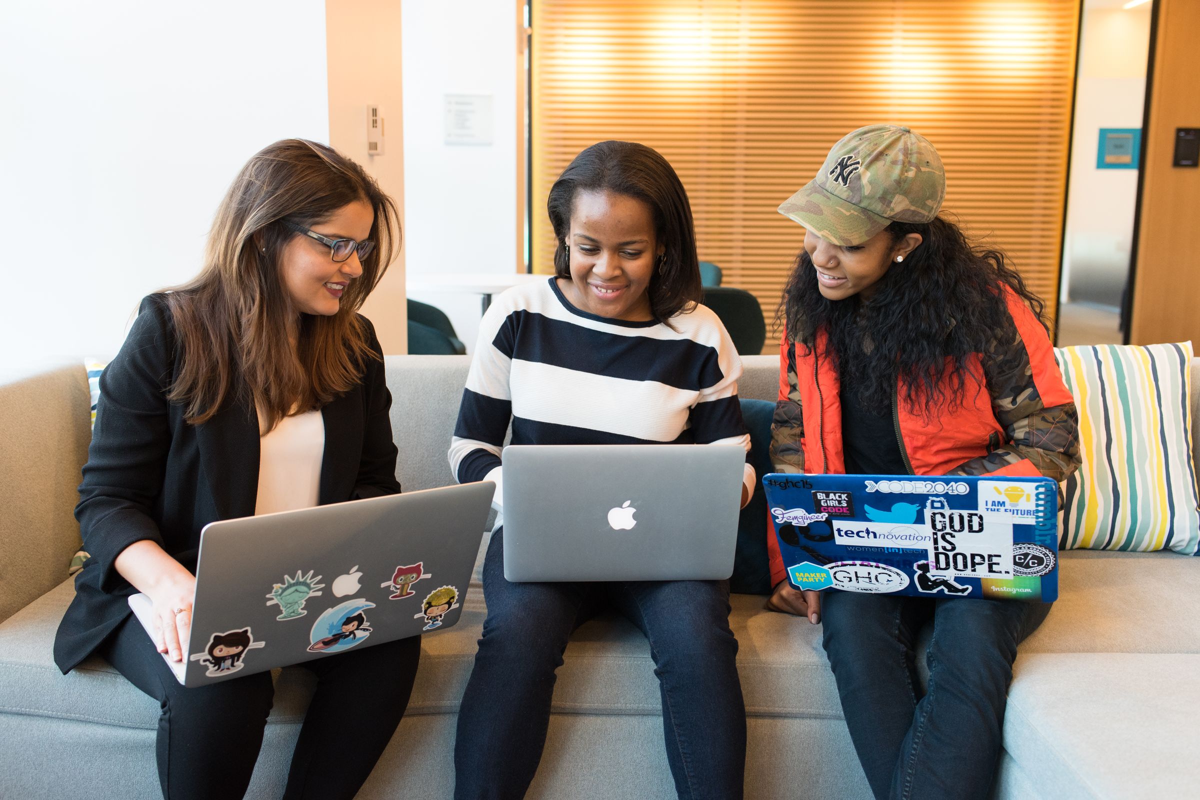 Three colleagues on a couch, laptops open, laughing